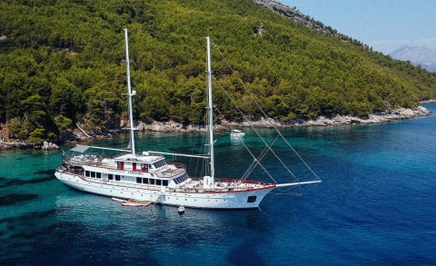 Corsario luxury yacht anchored near a rocky, pine-covered shoreline in turquoise waters
