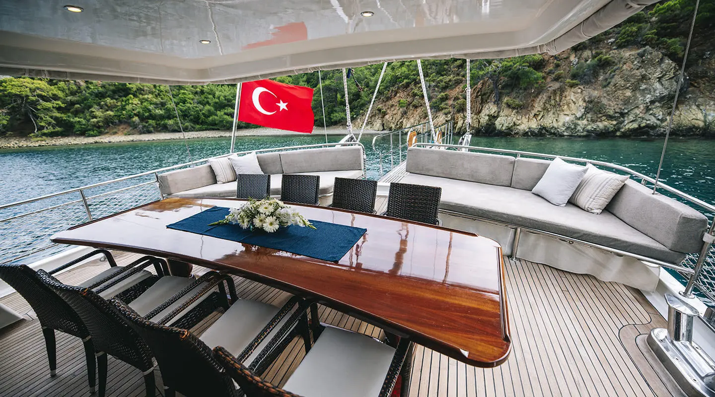 Kayhan 3 yacht deck with Turkish flag, wooden table, cushioned seating, sunset light
