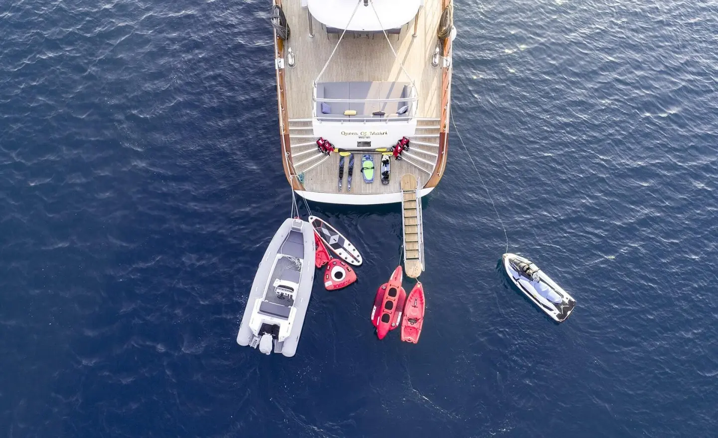 Aerial view of Queen Of Makri yacht at sea with two smaller boats nearby at sunset
