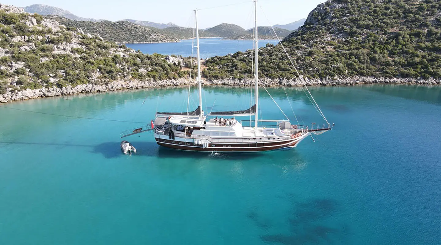 Prenses Esila yacht anchored in turquoise bay with cliffs, sailboat in background