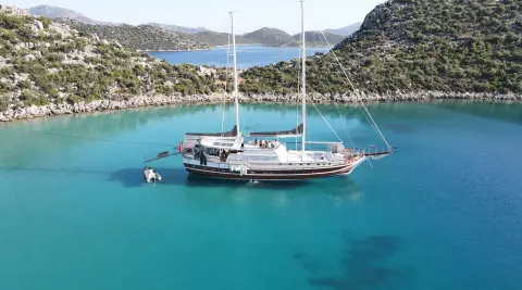 Prenses Esila yacht anchored in turquoise bay with cliffs, sailboat in background