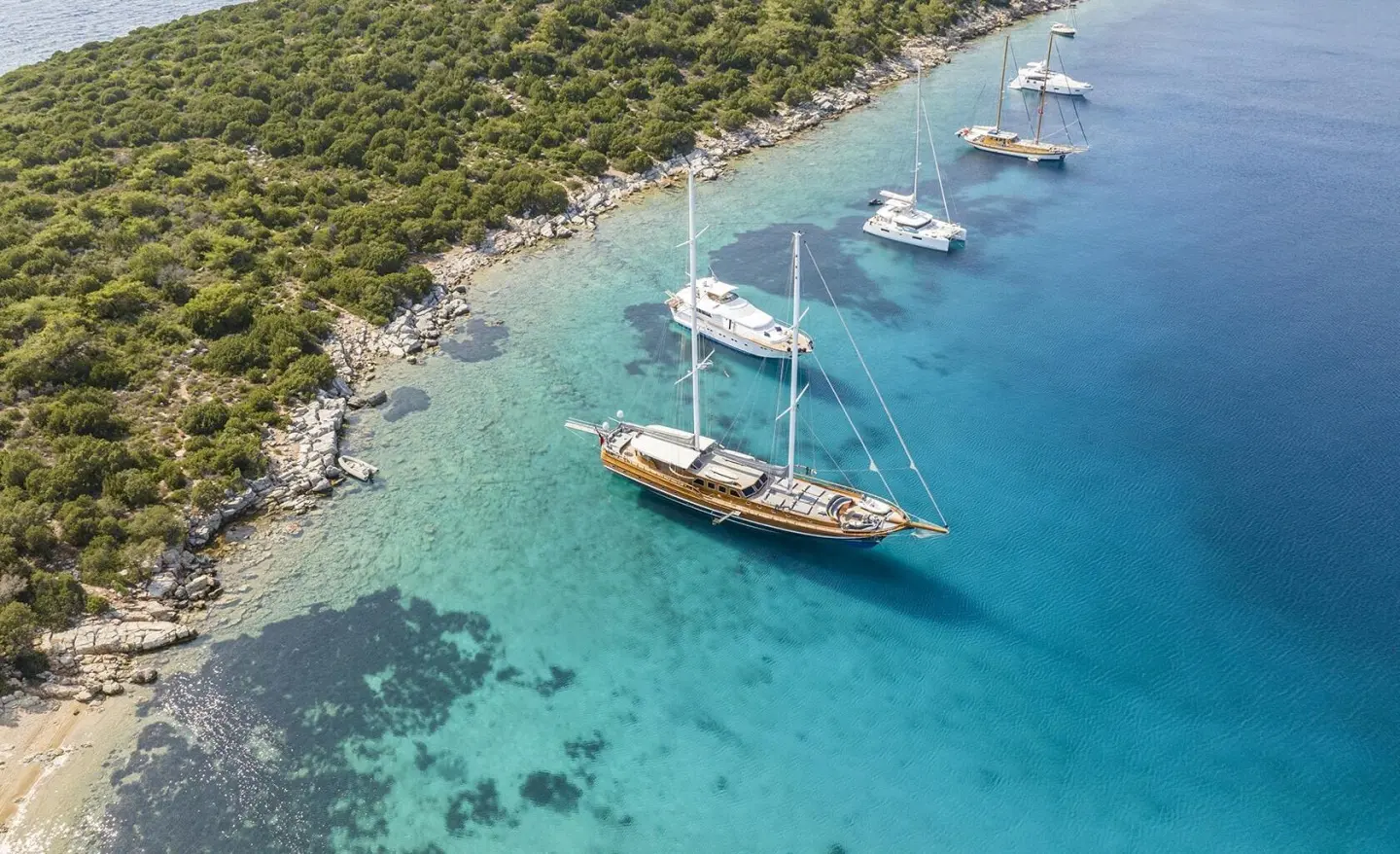 A luxury gulet yacht anchored in turquoise bay, with a rocky coastline