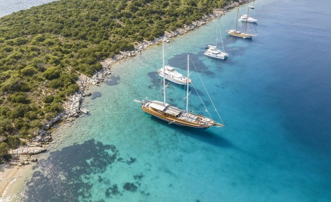 Bedia Sultan sailing yacht anchored near a rocky, pine-covered coastline with turquoise waters