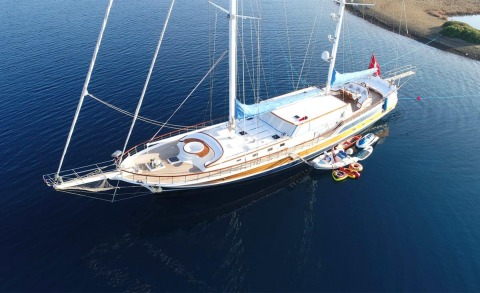 A luxury sailing yacht anchored on blue sea, with a white gulet-style hull, deck seating and sunbathing area