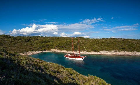 Red and white sailing yacht anchoring in a cove with green hills