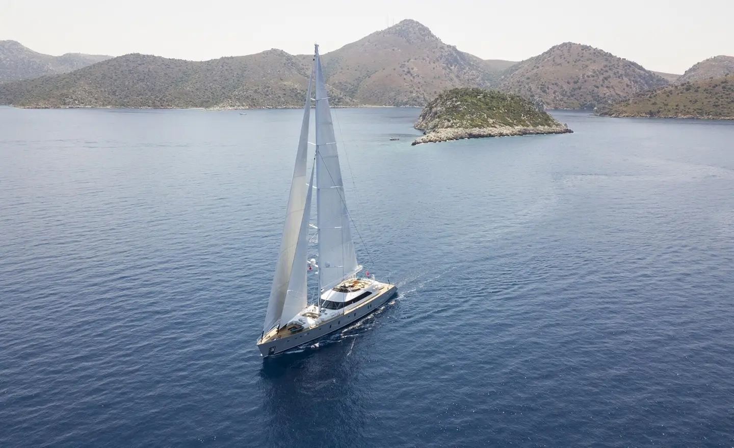 A white sailing yacht named All About U 2 glides across blue waters near rocky coastline