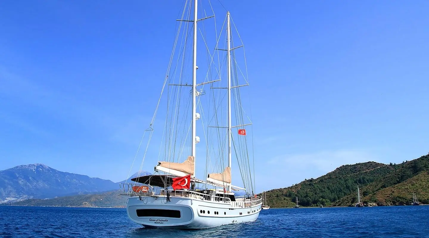 Two-masted sailing yacht on blue sea with distant mountains and coastline