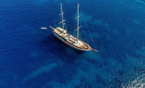 A 29m luxury sailing yacht Enderim A anchored in crystal blue calm sea, midship deck lounge and white sails folded aboard.