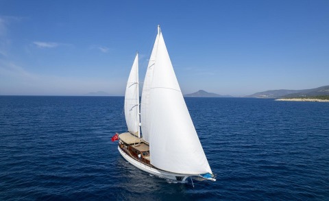 Arabella sailing yacht with white sails on deep blue sea, coastal backdrop and clear sky