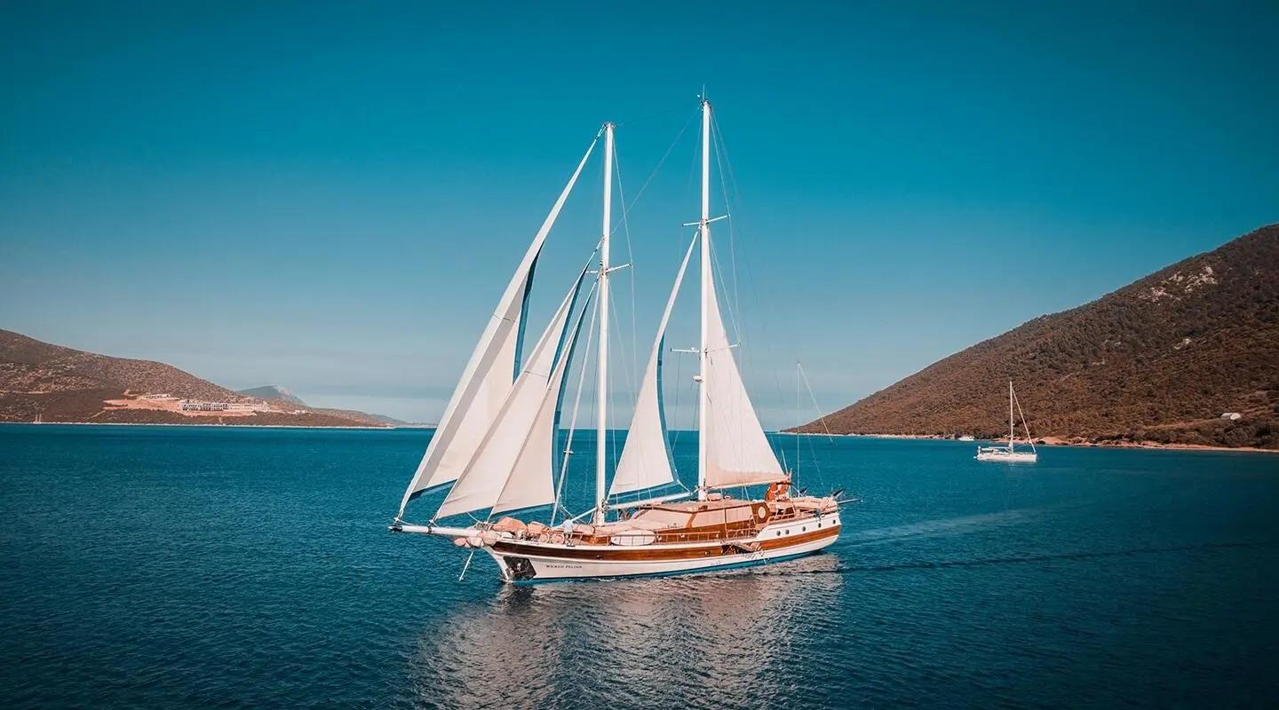 Sailing yacht Wicked Felina with white sails on blue sea at sunset