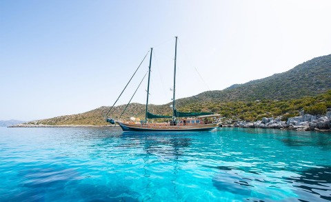 Ros Mare yacht anchored in turquoise waters near rocky shoreline and hills