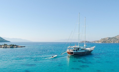 Two-masted luxury yacht anchored in clear blue sea with a small motorboat nearby