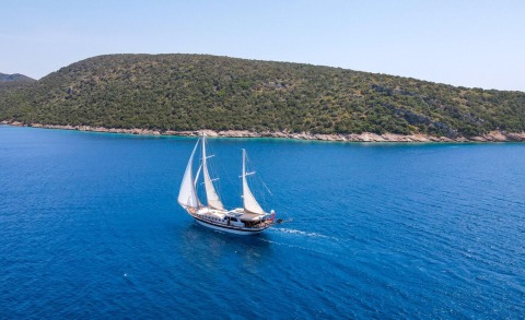 Gulet Ulucinar sailing alone on blue sea with rocky coastline in background