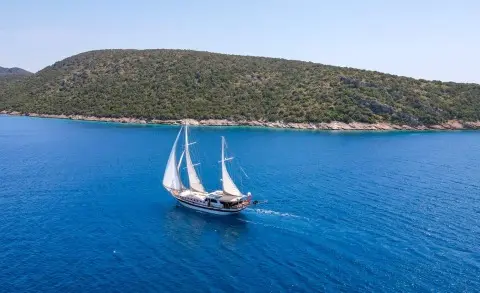 Gulet Ulucinar sailing alone on blue sea with rocky coastline in background