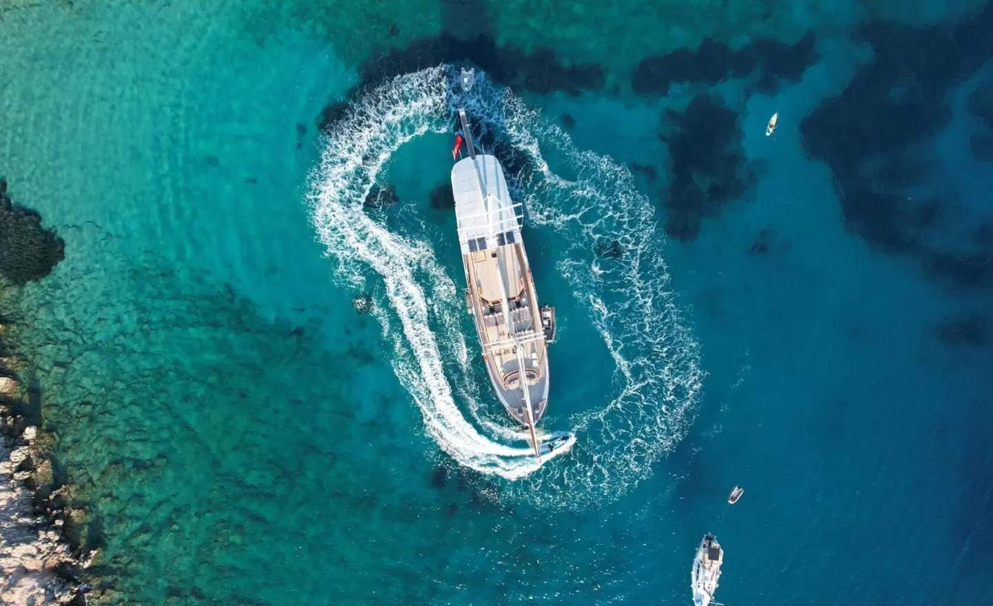 Aerial view of a blue and white gulet anchored in turquoise water near a rocky shoreline