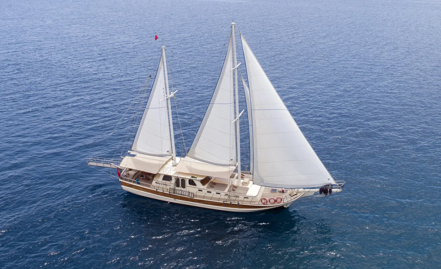 Faralya yacht sailing at sea with white sails and blue water, sunset vibe