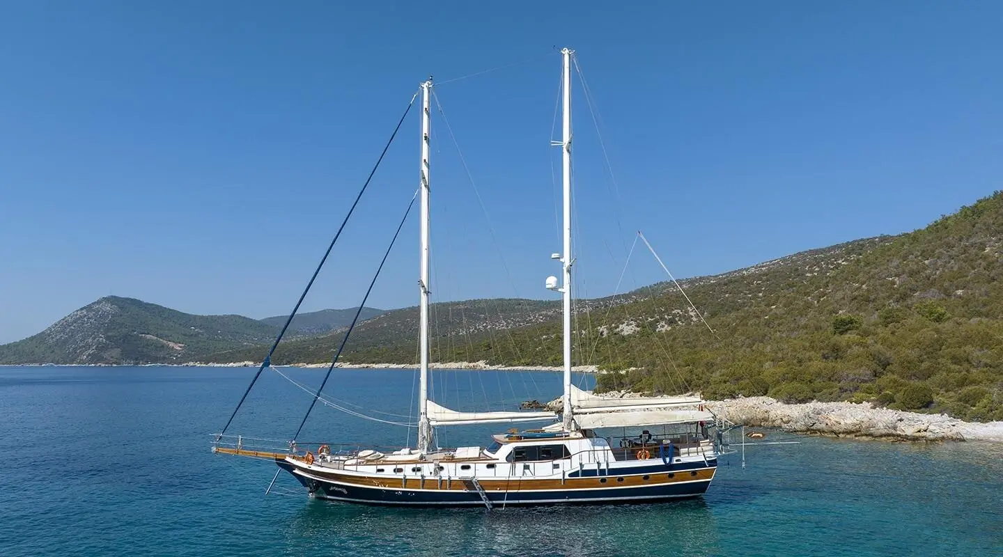 Gulet Artemis anchored in turquoise water with hills in the background