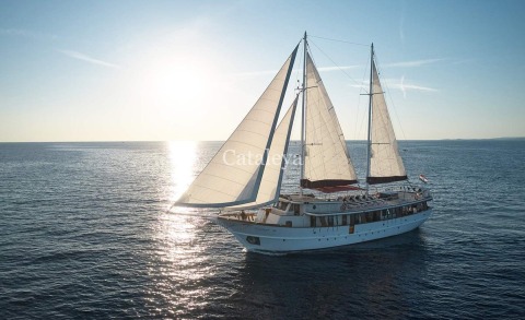 Sunlit sailboat Cataleya on calm sea with sails raised