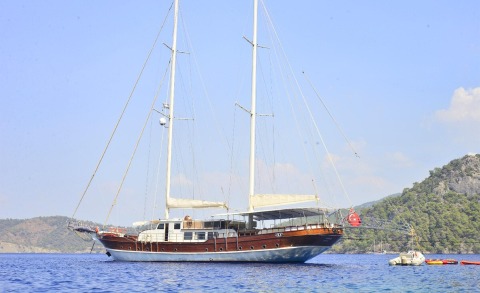 Luxurious wooden-hull sailing yacht anchored on blue sea with rigging and distant hills in the background