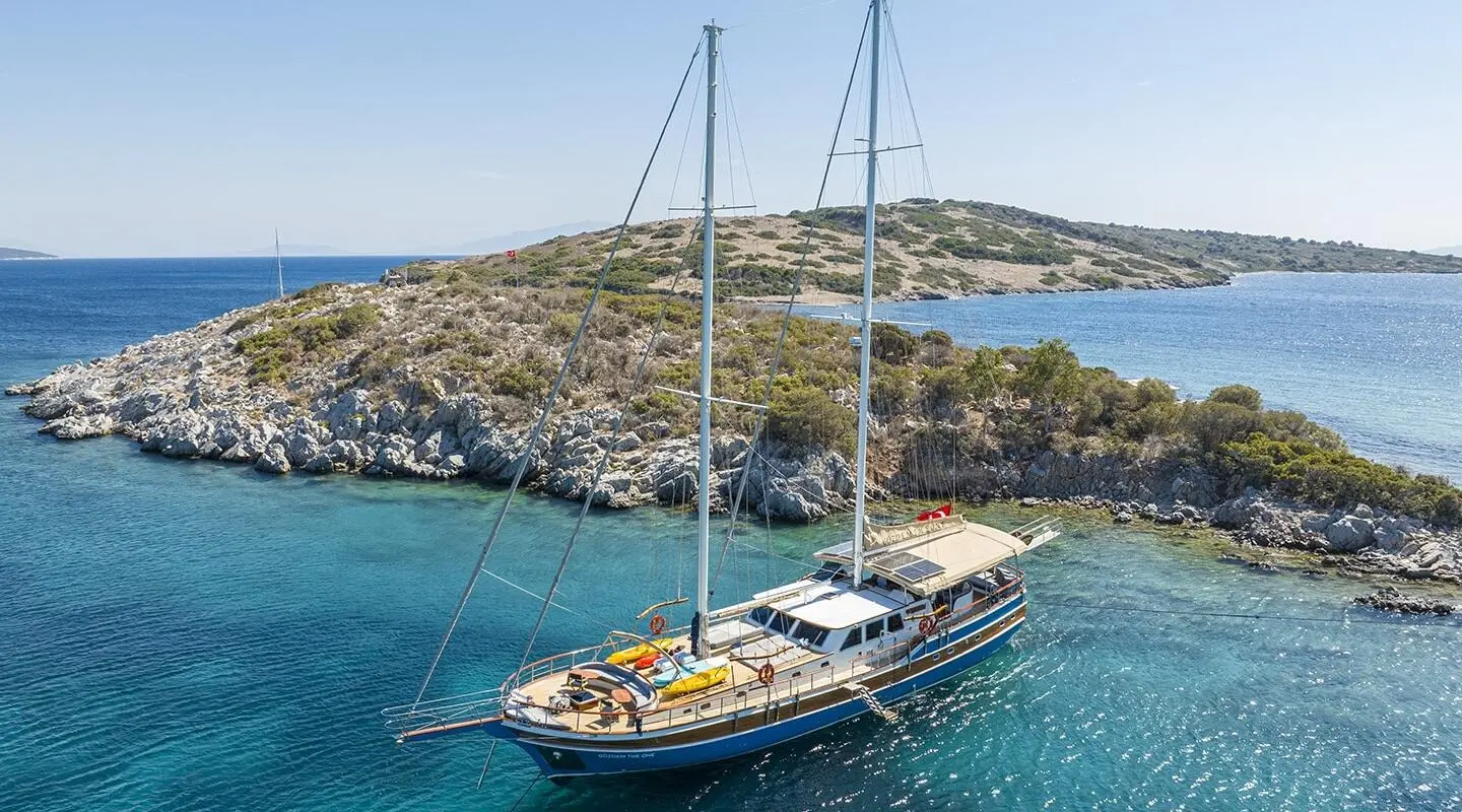 Gozdem The One yacht anchored in turquoise water with sailboat and hilly coastline