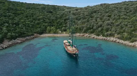Ros Mare yacht anchored near a green hillside, calm blue sea at sunset