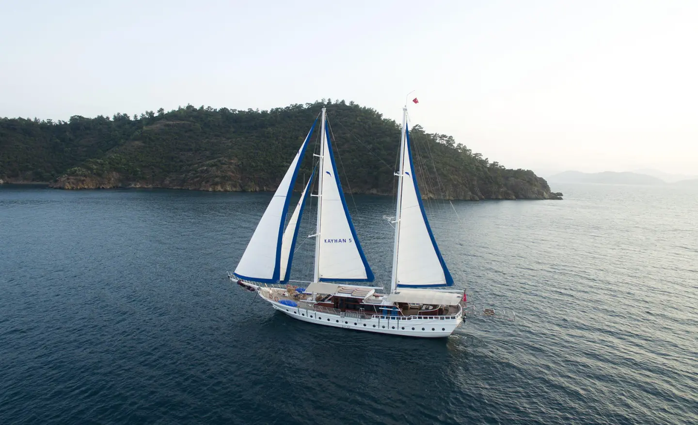 Kayhan 5 yacht sailing calm blue sea near hilly coastline at sunset