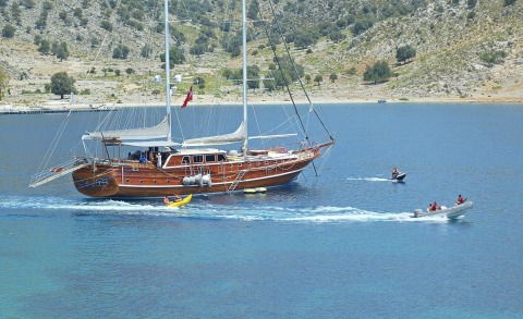 Wooden gulet yacht with two masts, people on deck, calm blue sea surroundings