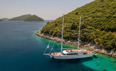 Love Story sailing yacht anchored near rocky green hillside coast