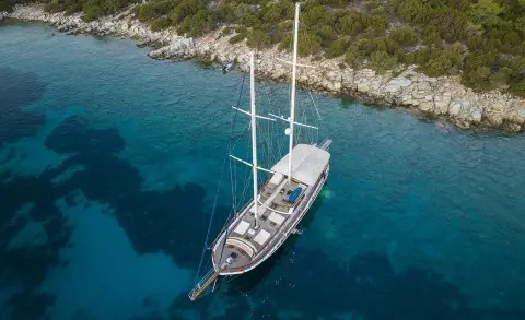 Artemis luxury yacht anchored near rocky shoreline at sunset