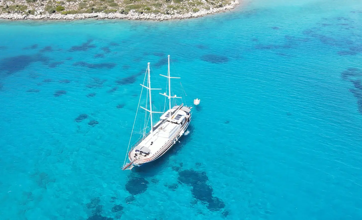 A white sailing yacht anchored in clear turquoise water near a rocky coastline