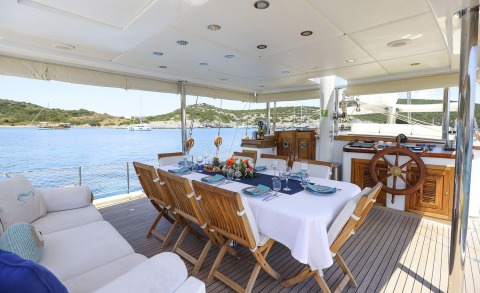 Wooden dining table and chairs on an open deck of Gazella yacht, sea and coastline view