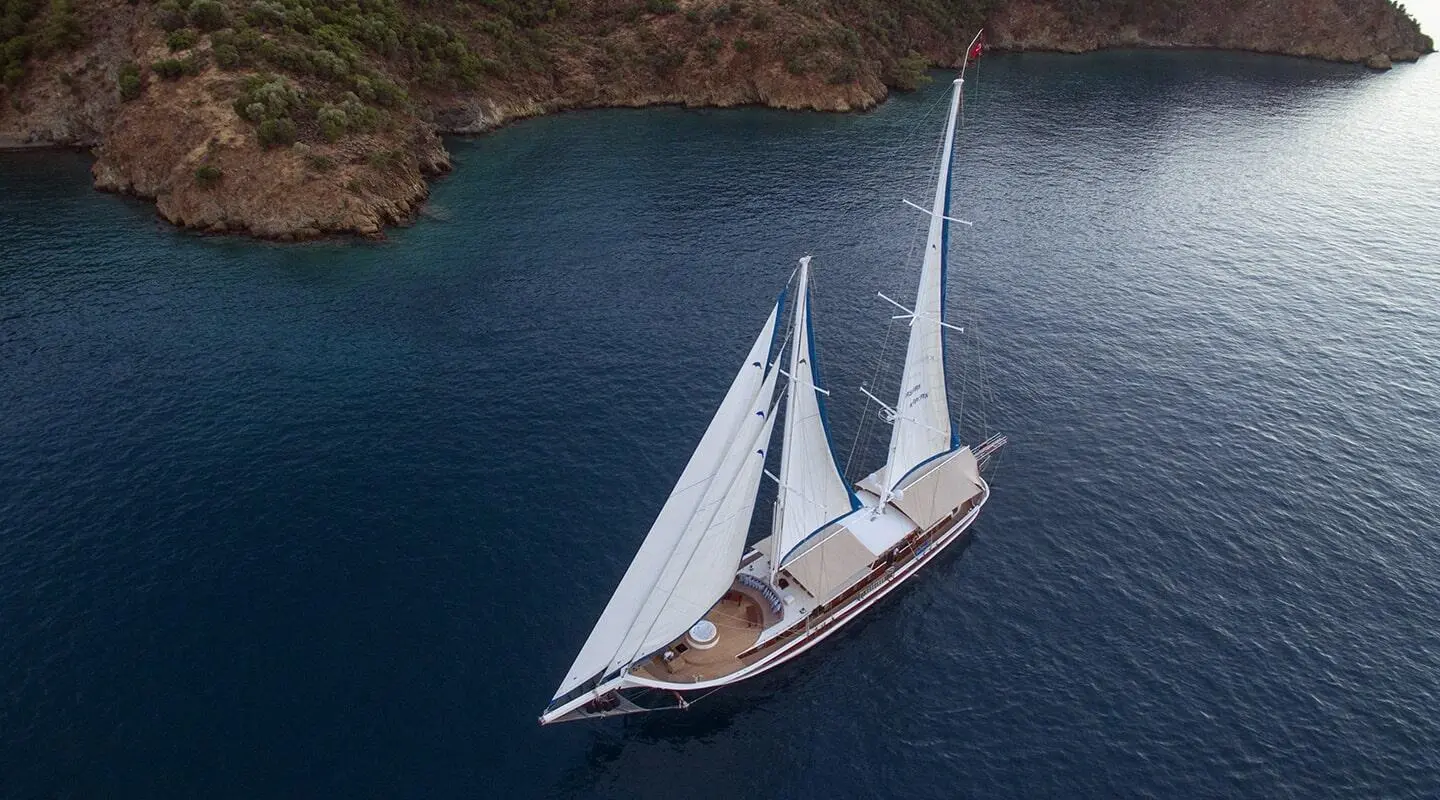 Kayhan Kaptan yacht sailing waters at sunset with sails full and rocky coastline