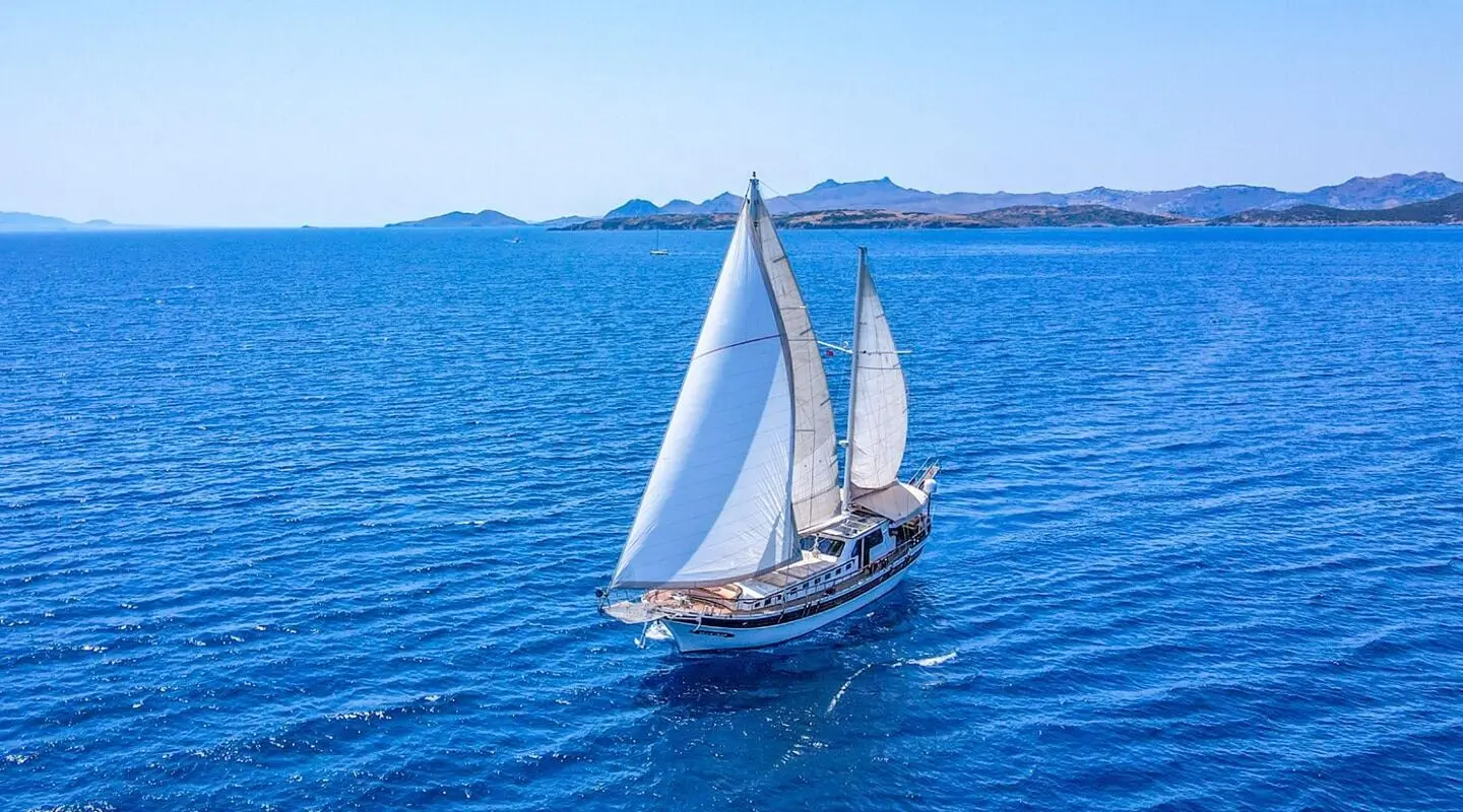 Ulucinar luxury gulet sailing at sunset with white sails on blue sea