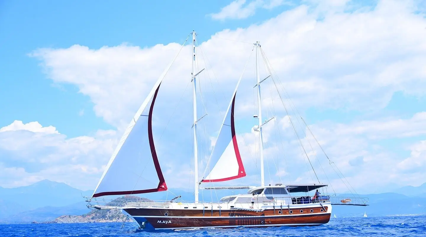 Maya luxury sailing yacht with white sails and dark wood hull on blue sea
