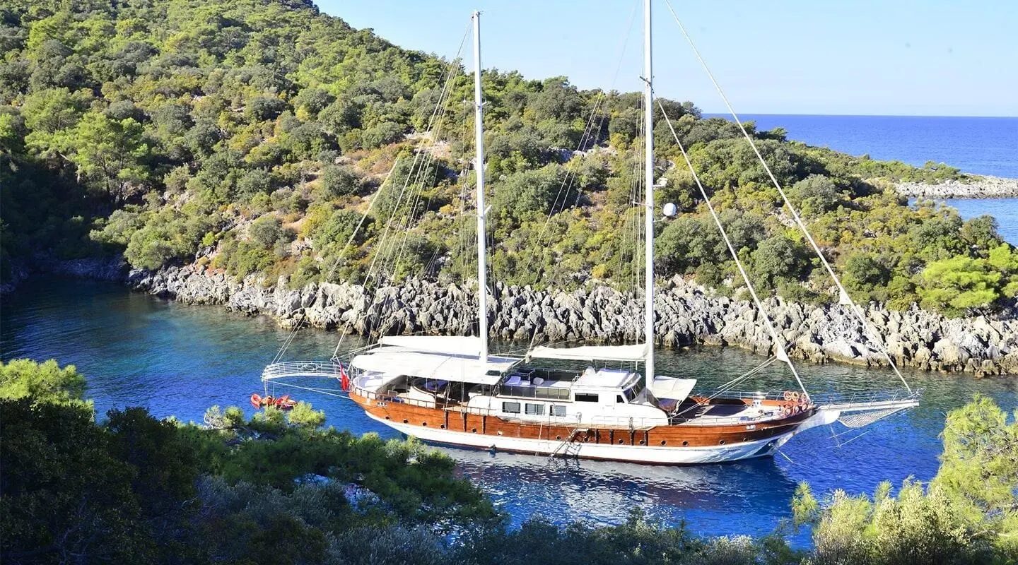 Yacht Berrak Su anchored near rocky coastline at sunset with sailboat