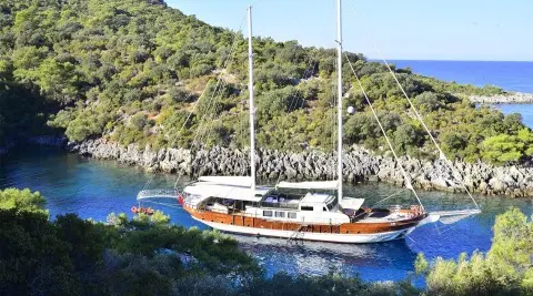 Yacht Berrak Su anchored near rocky coastline at sunset with sailboat