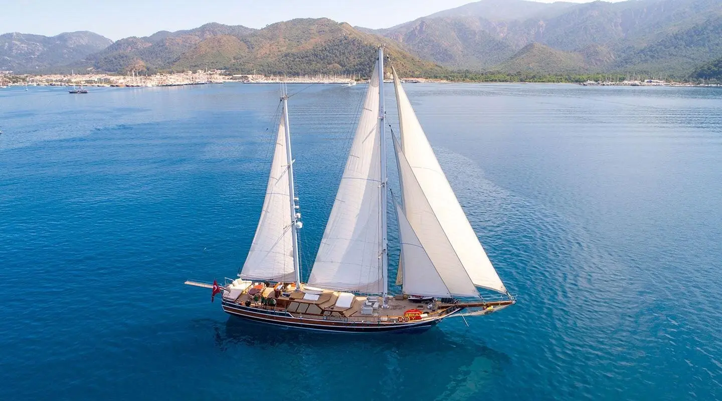 Grande Mare sailing yacht anchored in turquoise sea near a coastal town and mountains