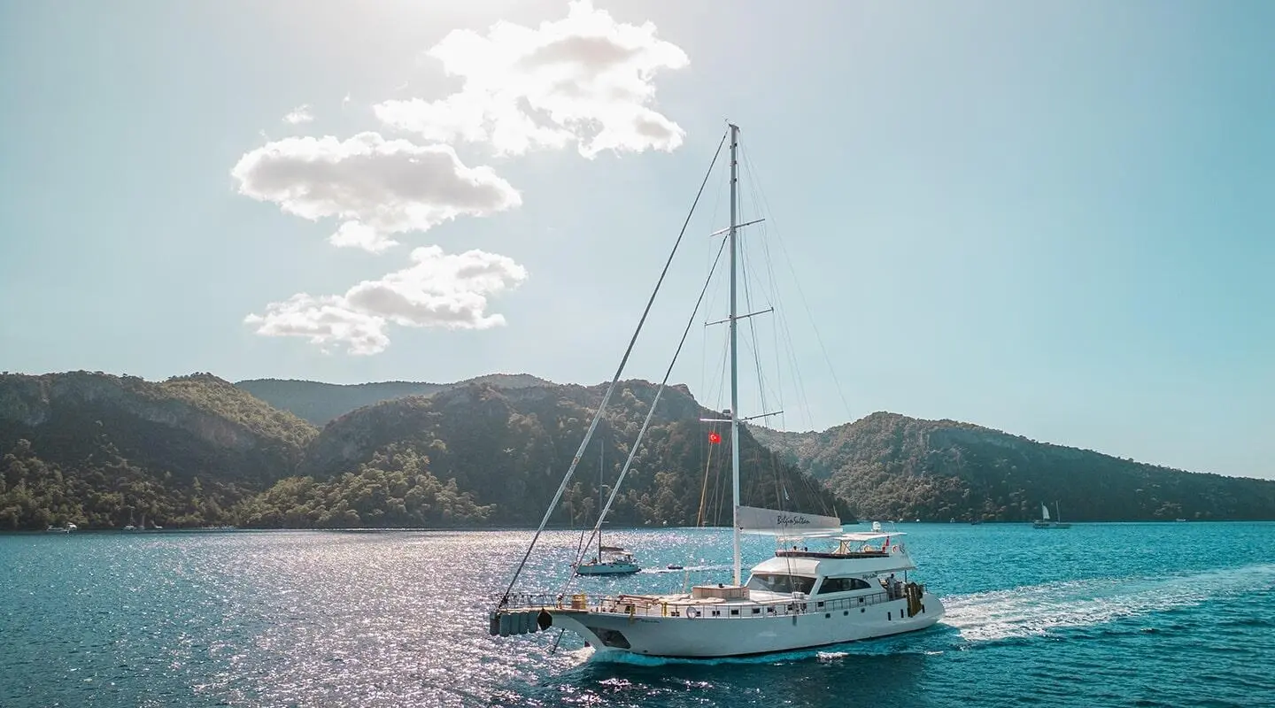 Belgin Sultan yacht anchored near hilly coastline at sunset with sails down
