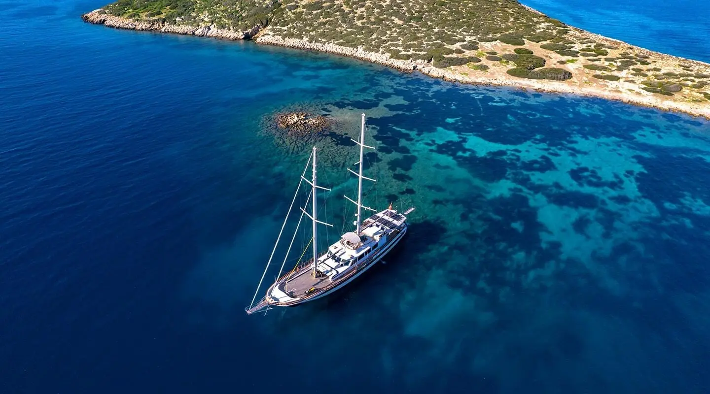 Double Eagle yacht anchored near coastline with blue waters and a sunlit horizon