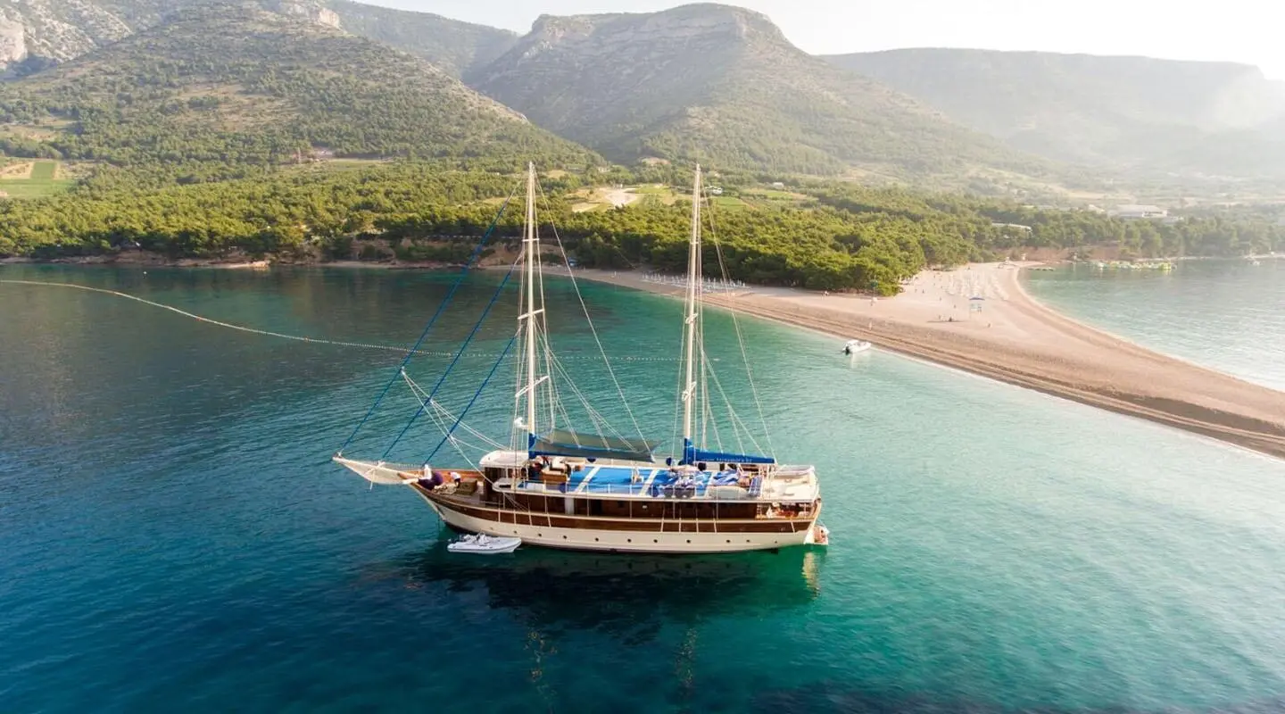 Gulet Tajna Mora anchored in turquoise bay with clear water and sandy shore