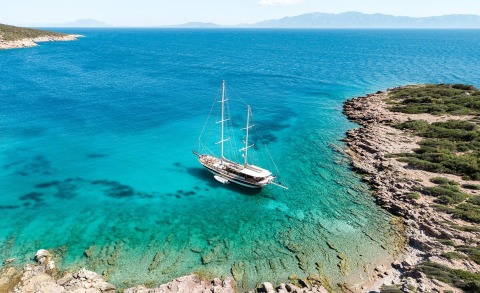 Sailing yacht anchored in turquoise sea near rocky coastline at sunset