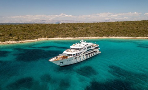 A large white yacht anchored in turquoise waters near a sandy coastline on a sunny day