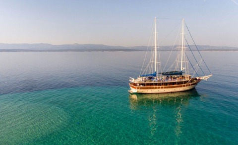 A wooden gulet yacht with sails on open sea, visible deck and masts