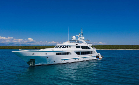 Alalya luxury motor yacht anchored in turquoise sea with coastline in background