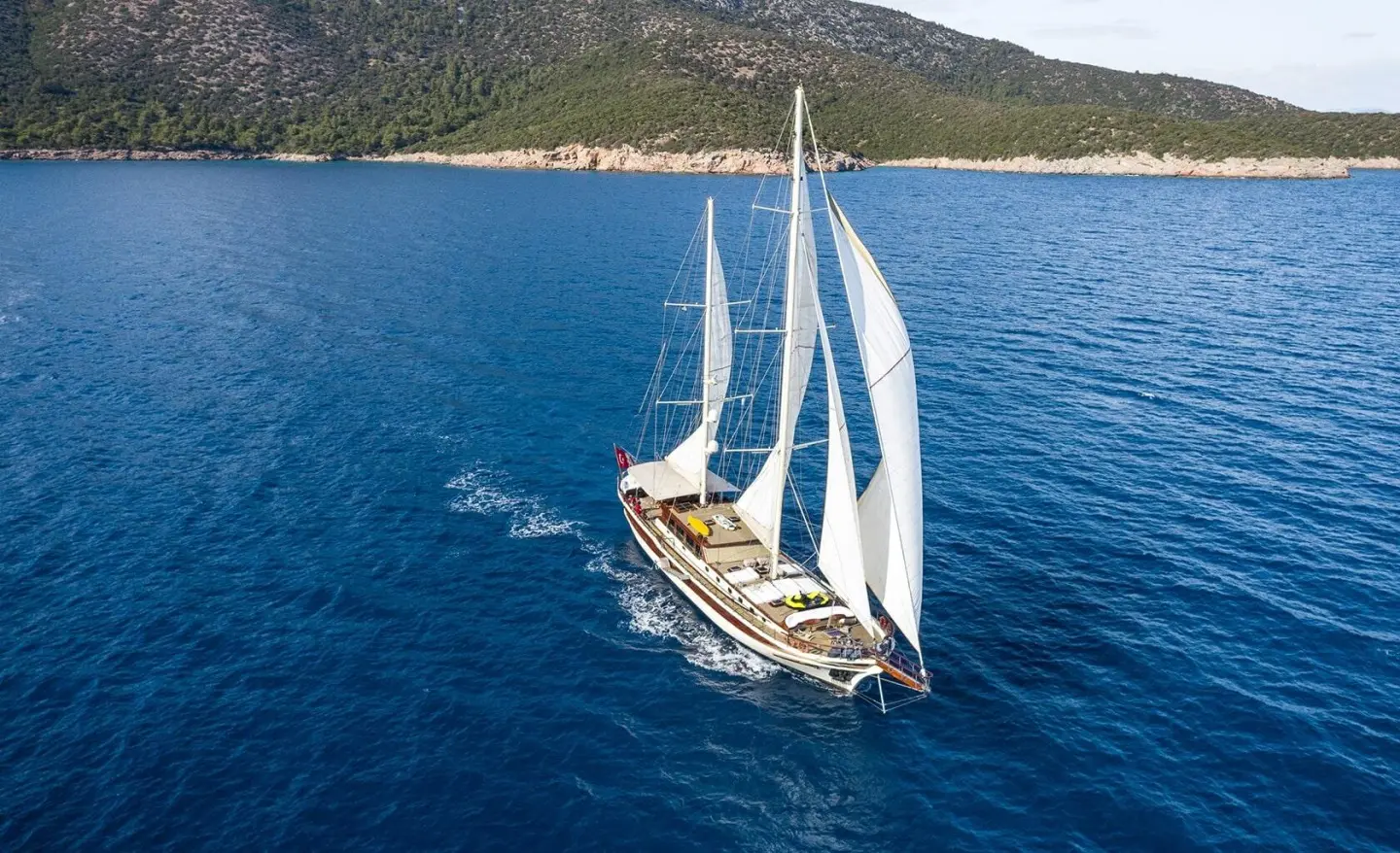 Gulet Estrella De Mar sails near the turquoise sea, white sails unfurled, blue water