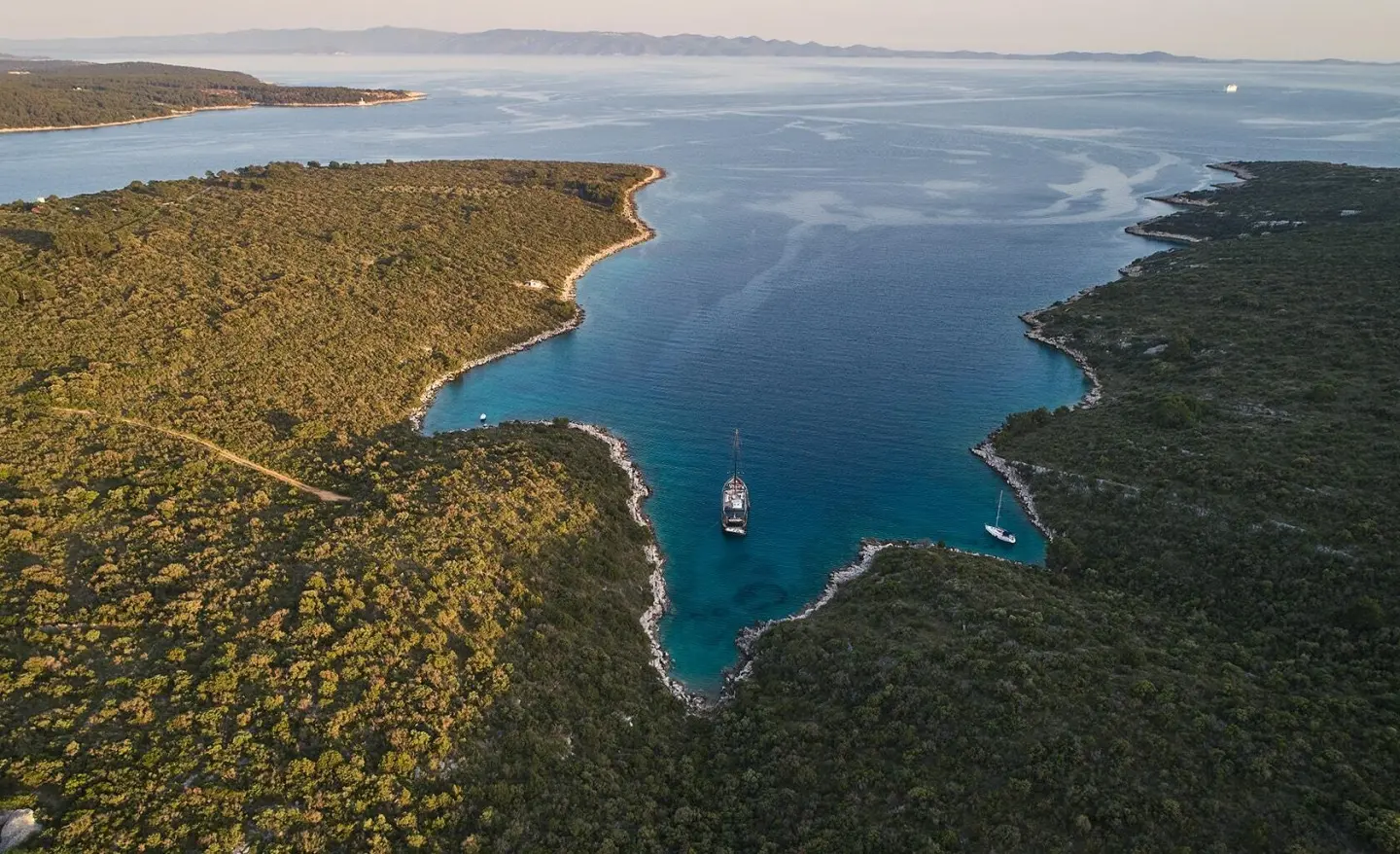 Sunset-lit luxury gulet named Rara Avis anchored by rugged coast, calm sea