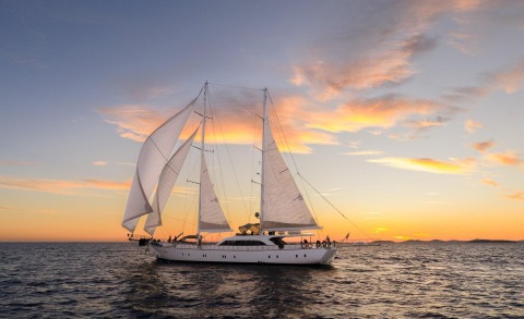 Luxurious sailing yacht at sunset on open sea with sails raised
