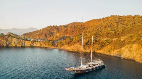 Gulet Esma Sultan anchored along coastline with rocky cliffs in sunset light