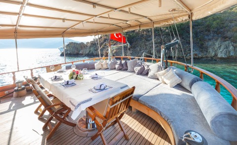 Deck dining area with place settings on table, red Turkish flag, rocky coast and blue water visible