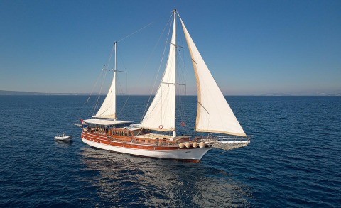 Elegant wooden two-masted sailing yacht at sea with white sails and a brown hull